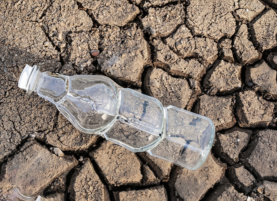 Garrafa de água cristalina em solo seco  e rachado