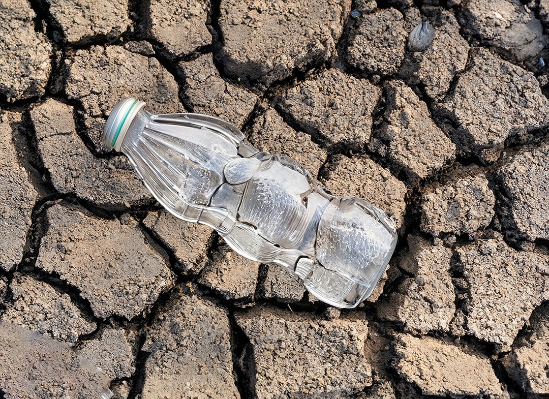 Garrafa de água cristalina em solo seco  e rachado