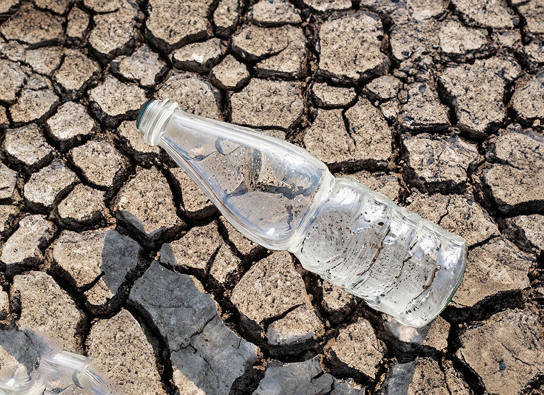 Garrafa de água cristalina em solo seco  e rachado