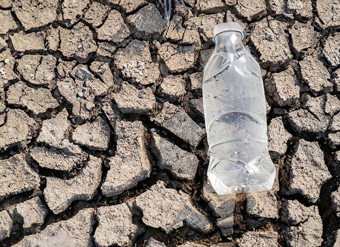 Garrafa de água cristalina em solo seco  e rachado