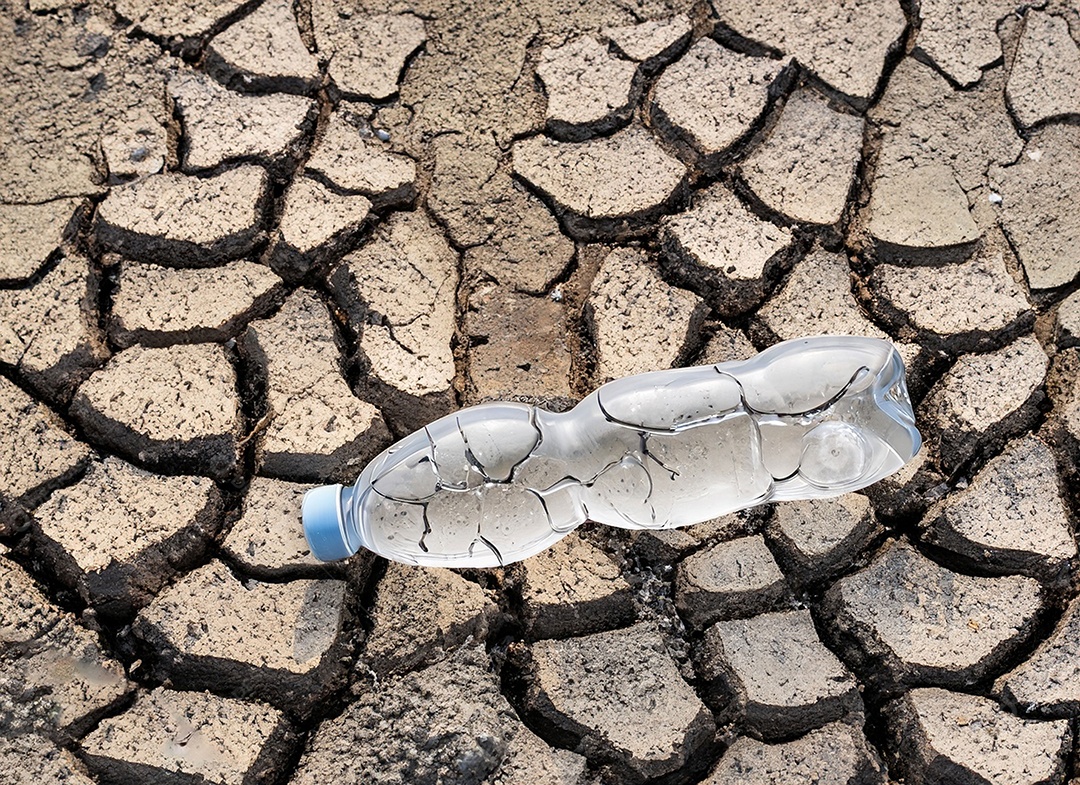 Garrafa de água cristalina em solo seco  e rachado