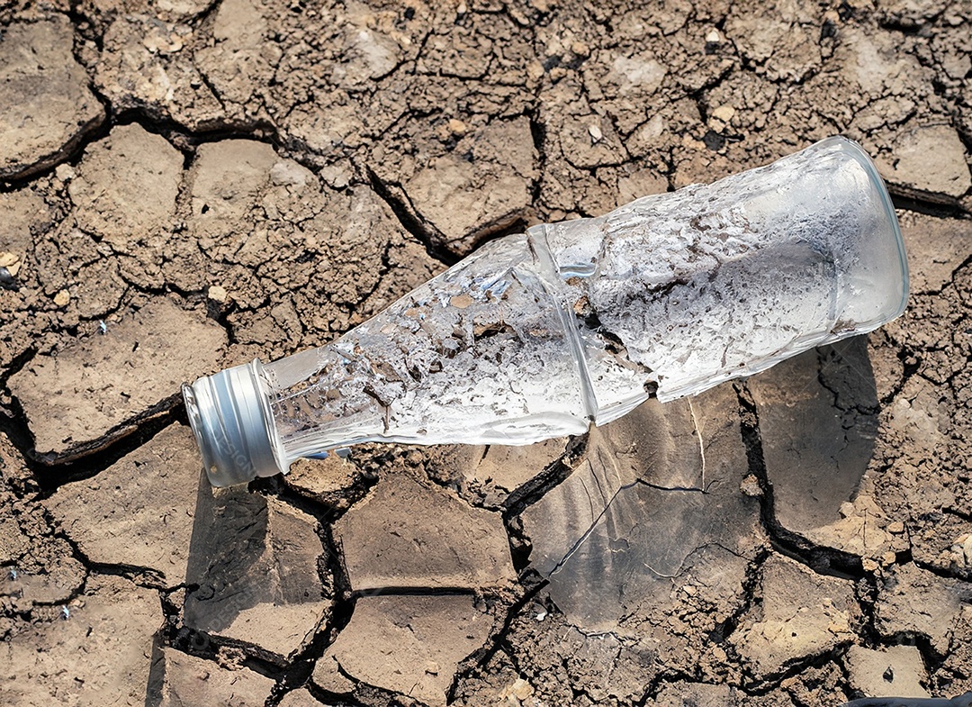 Garrafa de água cristalina em solo seco  e rachado