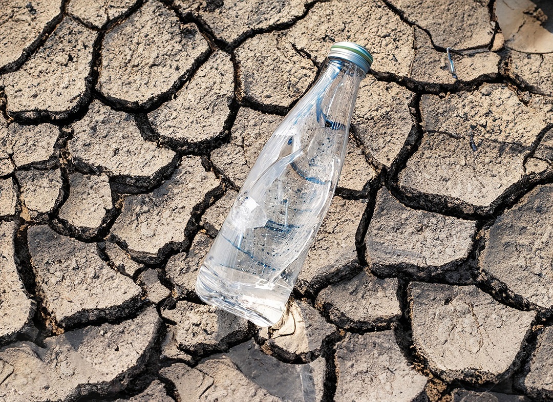 Garrafa de água cristalina em solo seco  e rachado