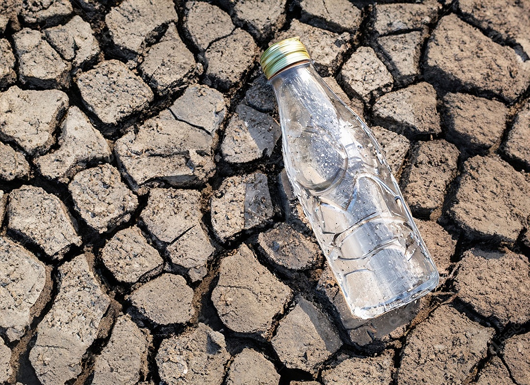 Garrafa de água cristalina em solo seco  e rachado