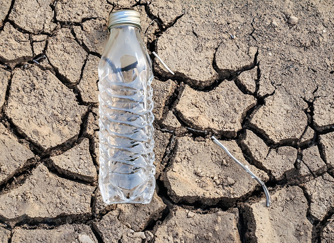 Garrafa de água cristalina em solo seco  e rachado
