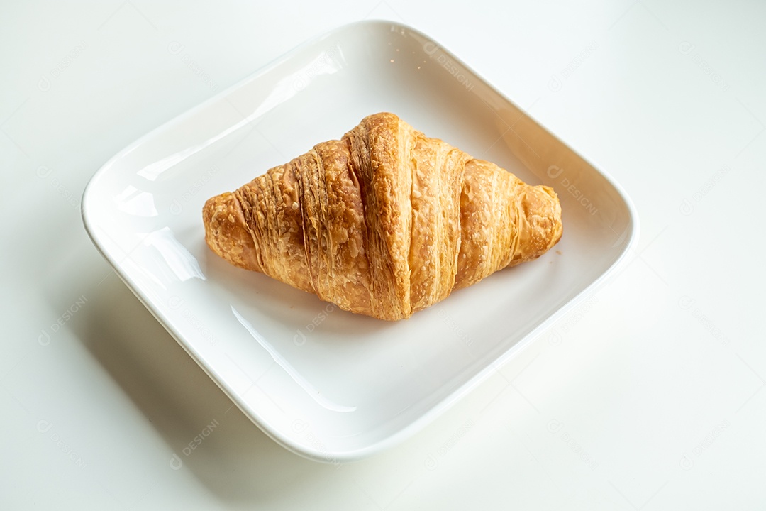 Pão croissant em um prato branco está sobre uma mesa branca
