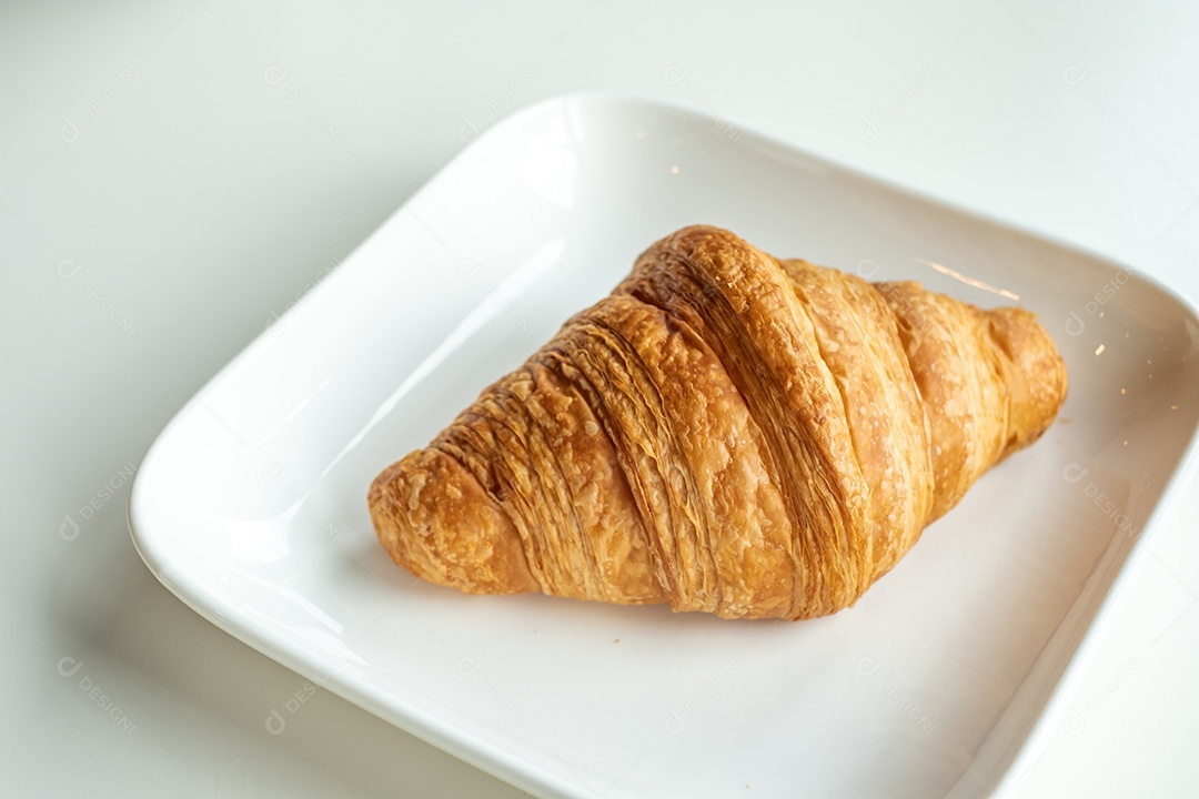 Pão croissant em um prato branco está sobre uma mesa branca