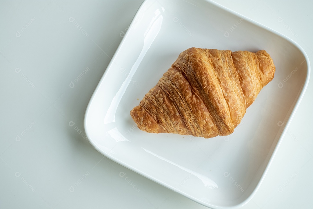 Pão croissant em um prato branco está sobre uma mesa branca