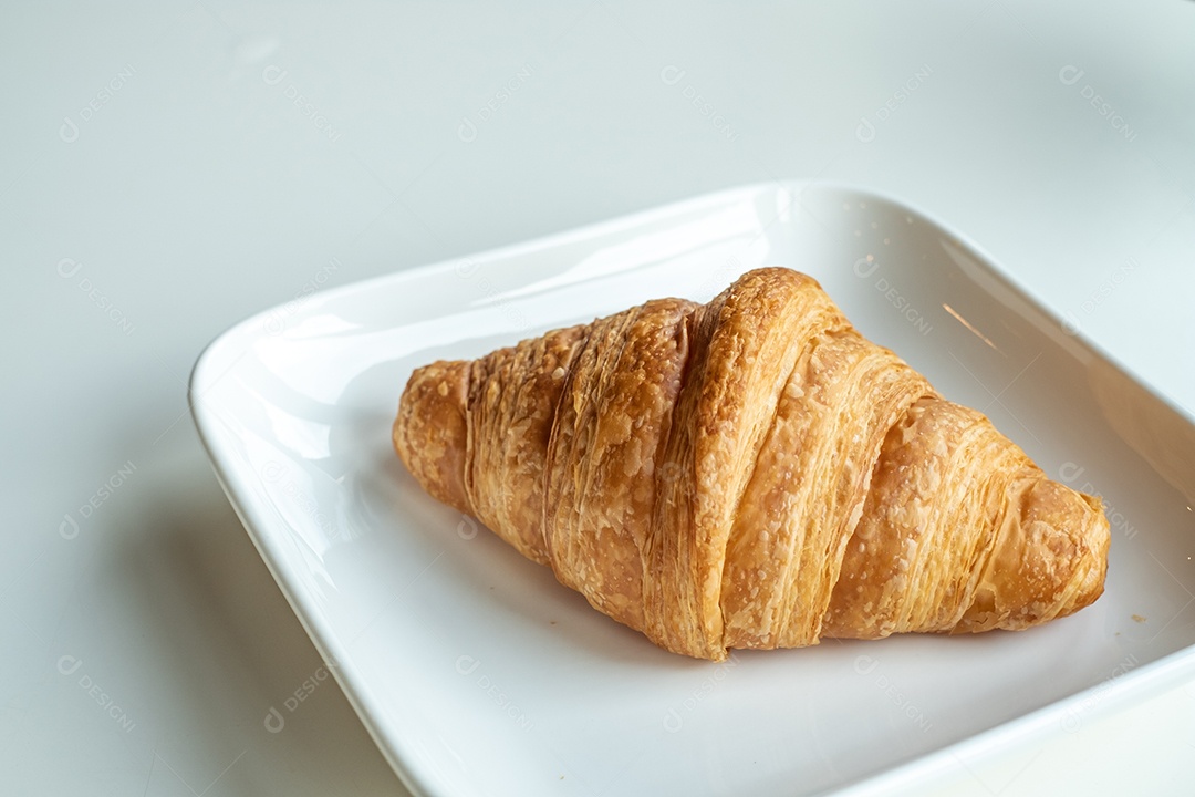 Pão croissant em um prato branco está sobre uma mesa branca