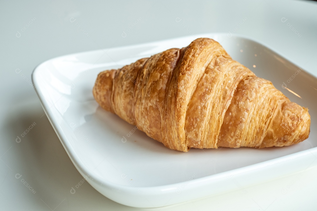 Pão croissant em um prato branco está sobre uma mesa branca
