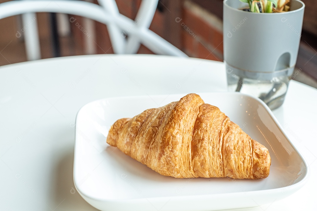 Pão croissant em um prato branco está sobre uma mesa branca