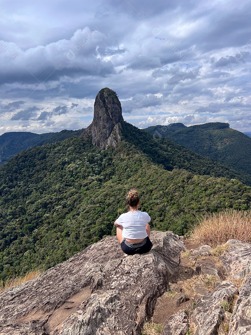 Mulher sentada admirando paisagem linda em cima de uma montanha.