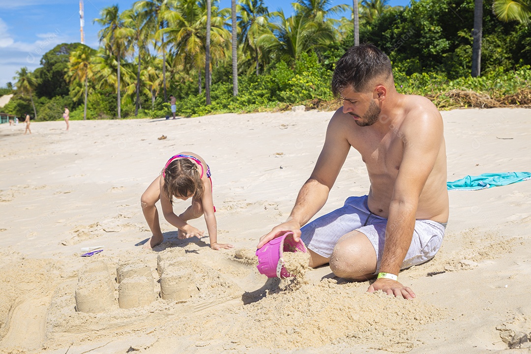 Homem e menina brincando na areia da praia