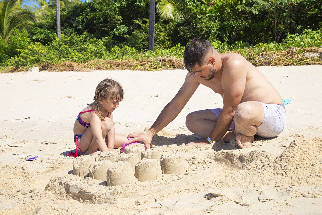 Homem e menina brincando na areia da praia