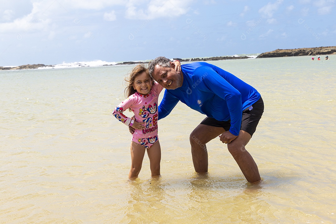 Pai e filha sorridentes curtindo na praia