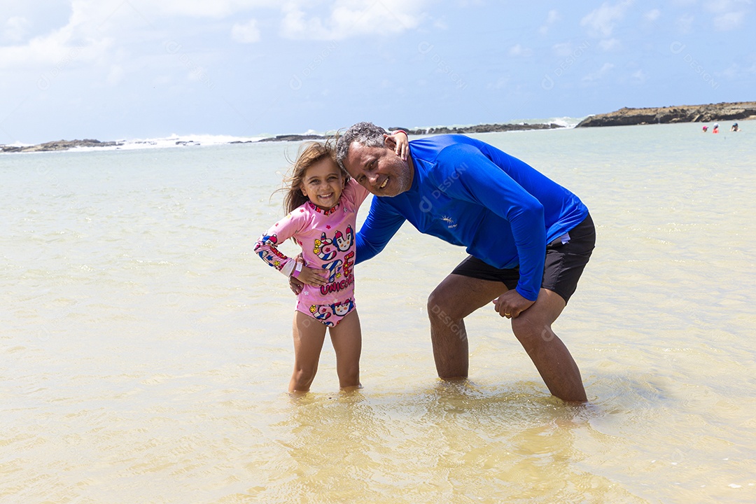 Pai e filha sorridentes curtindo na praia