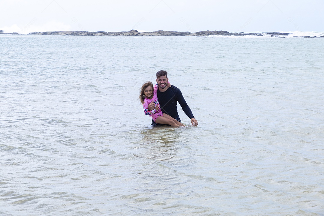Pai e filha sorridentes curtindo na praia
