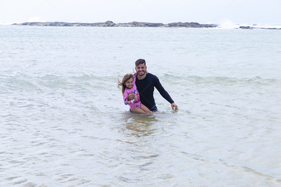 Pai e filha sorridentes curtindo na praia