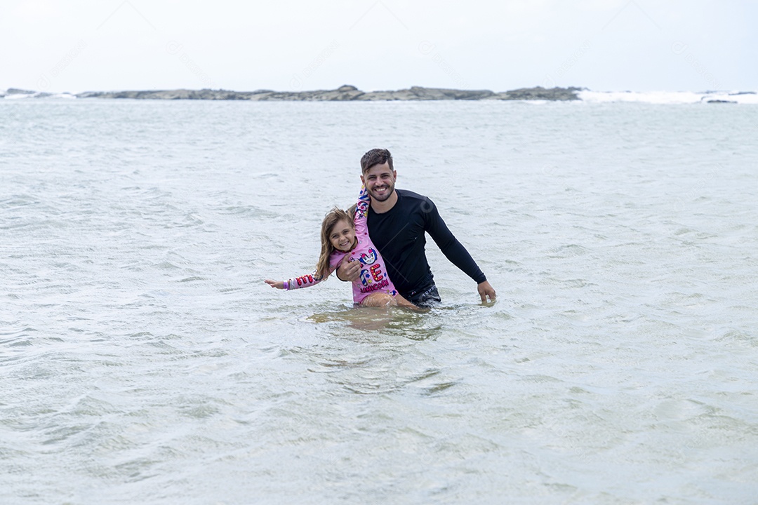 Pai e filha sorridentes curtindo na praia