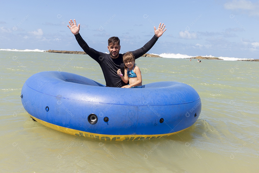 Pai e filha sorridentes brincando com boia azul na praia