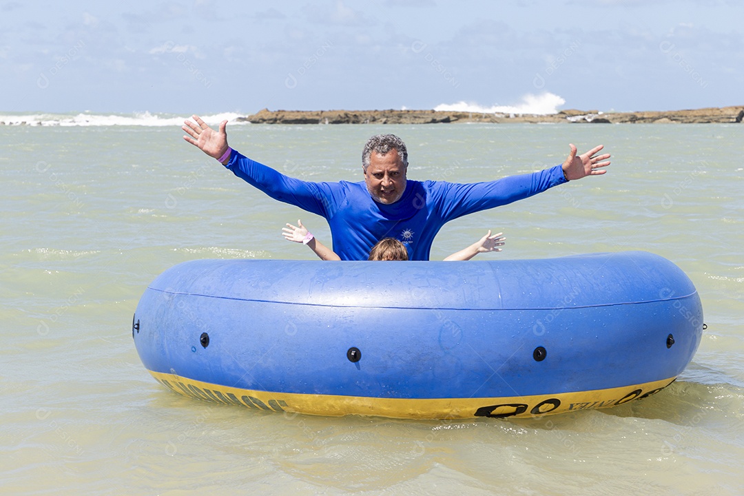 Homem sorridente brincando com boia azul na praia