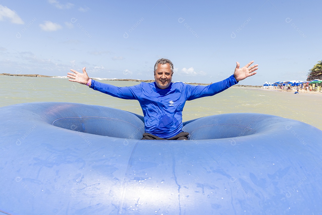 Homem sorridentes brincando com boia azul na praia