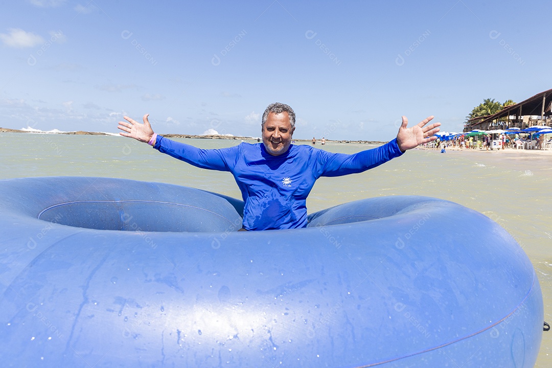 Homem sorridentes brincando com boia azul na praia