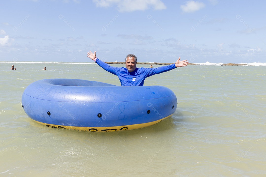 Homem sorridentes brincando com boia azul na praia