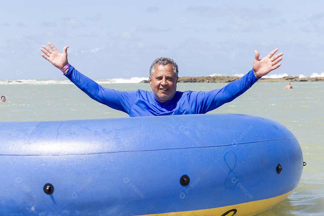 Homem sorridentes brincando com boia azul na praia