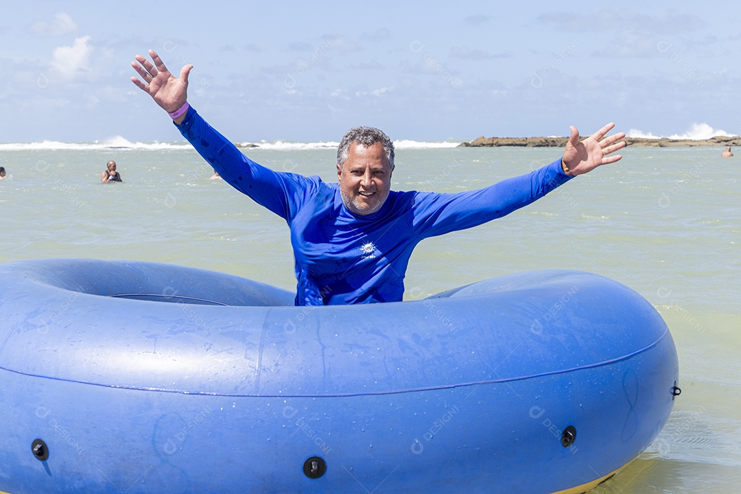 Homem sorridentes brincando com boia azul na praia