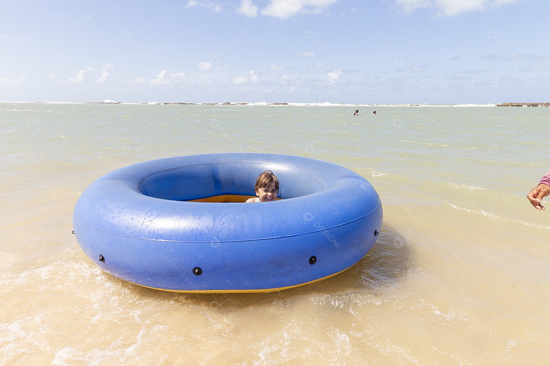 Menina sorridente brincando com boia azul na praia