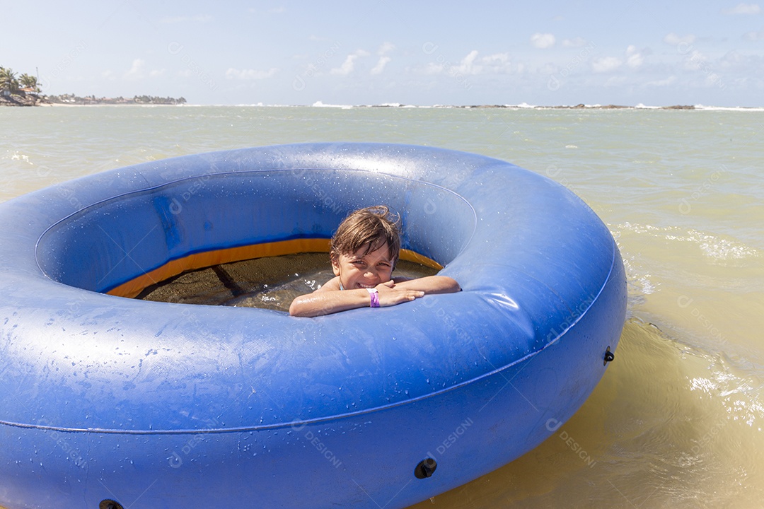 Menina sorridente brincando com boia azul na praia