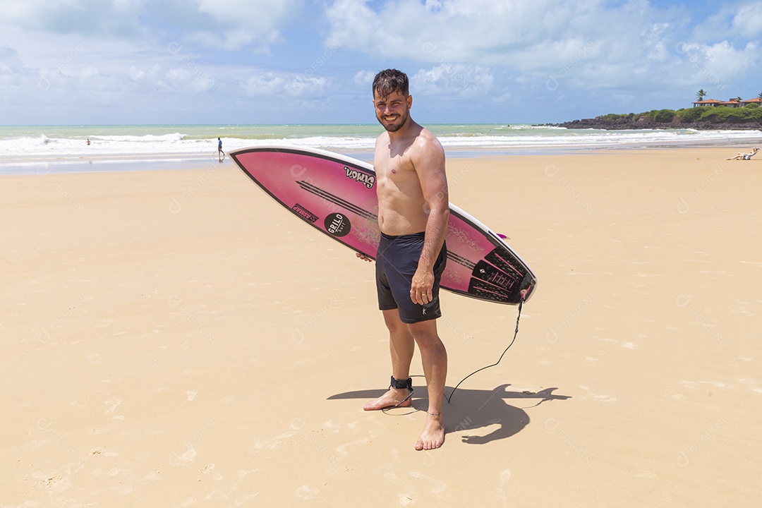 Homem jovem sorridente com prancha de surf na praia