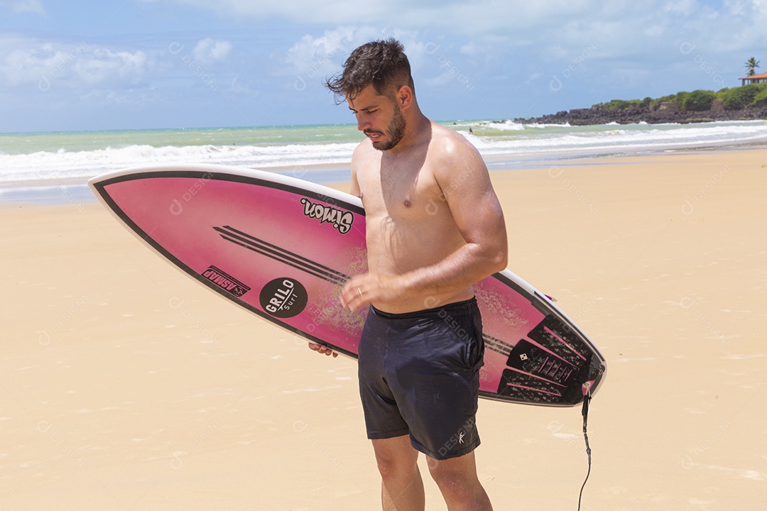 Homem jovem sorridente com prancha de surf na praia