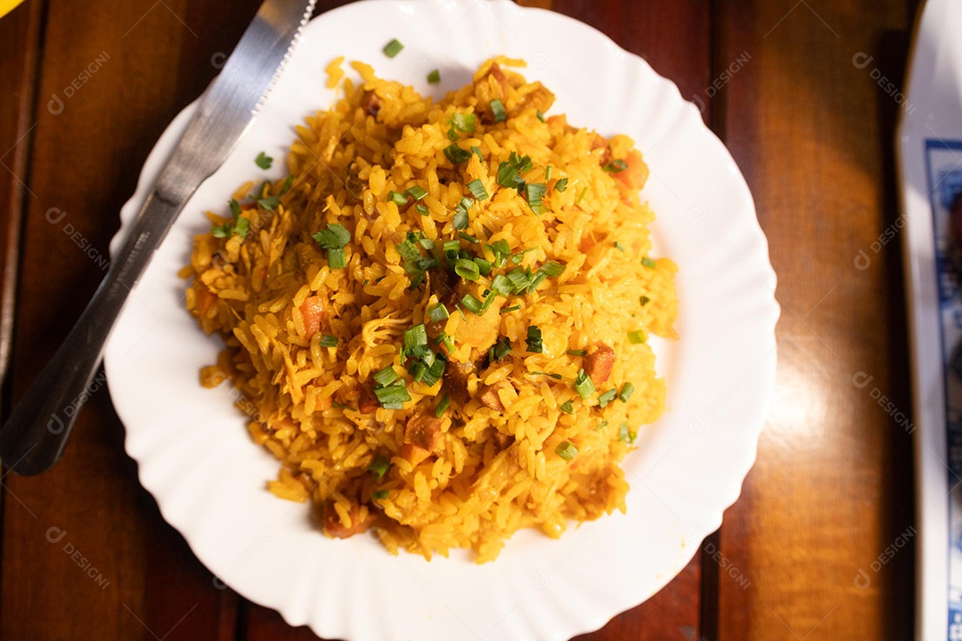 Um prato de galinhada sobre uma mesa de madeira