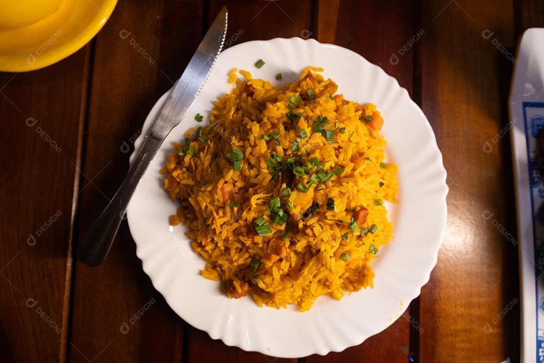 Um prato de galinhada sobre uma mesa de madeira