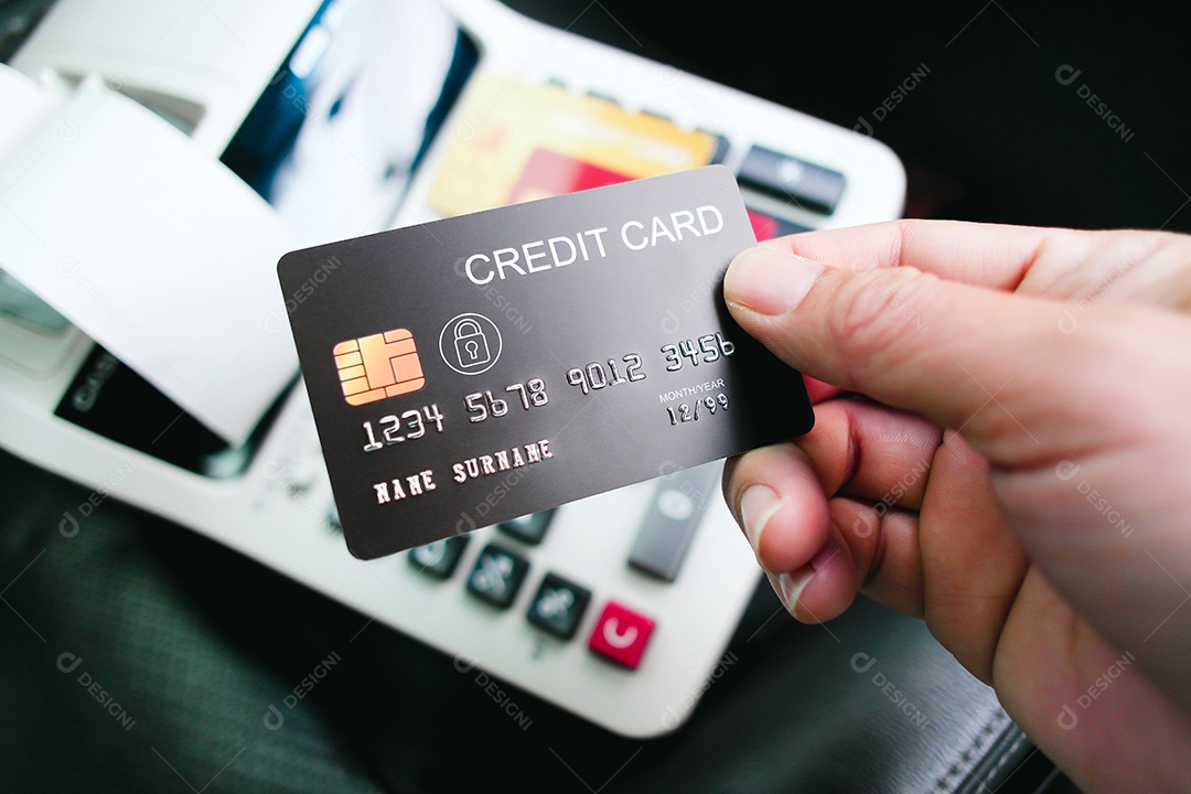 Mão segurando cartão de crédito com uma calculadora sobre o fundo