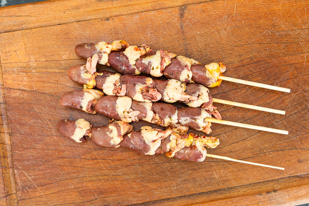 Espetinhos de coração de galinha sobre tábua de madeira