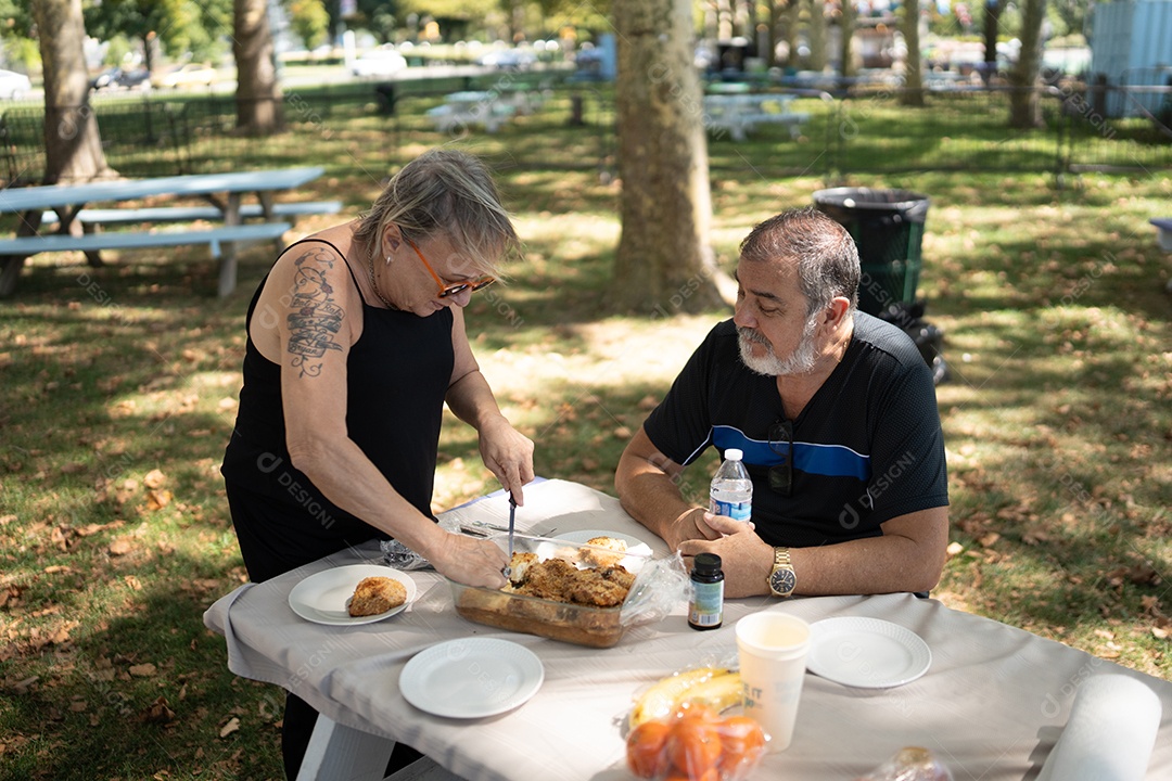 Amigos adultos se unindo para comer em um piquenique ensolarado ao ar livre.