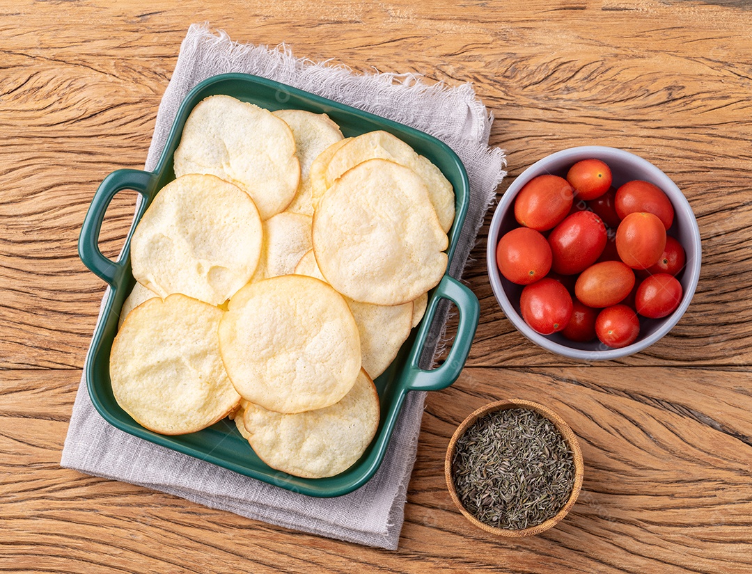 Lascas de queijo provolone defumado em uma tigela com tomate cereja e orégano sobre a mesa de madeira.