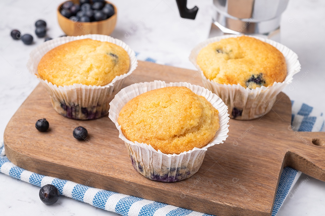Muffins de mirtilo com frutas sobre tábua de madeira.