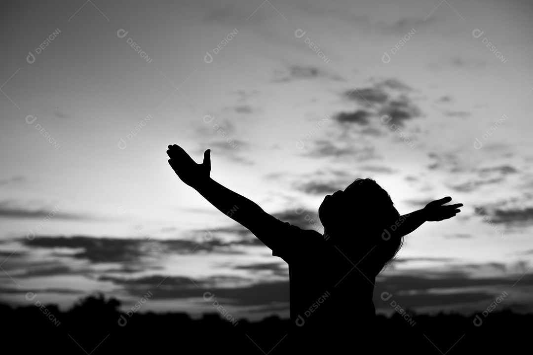 Silhueta de uma garota observando o pôr do sol laranja e o fundo turvo do céu dourado e azul com braços abertos