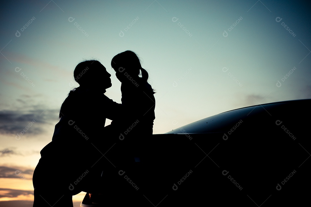 Silhueta de uma garota observando o pôr do sol laranja e o fundo turvo do céu dourado e azul com braços abertos