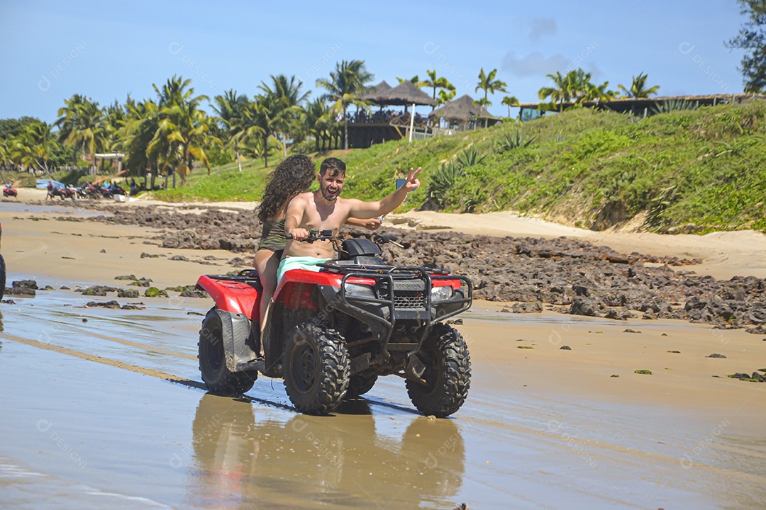 Casal de jovens sorridentes andando de quadriciclo pela praia