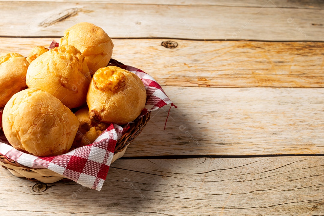 Pães de queijo em cesta sobre mesa de madeira