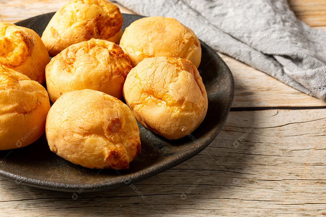 Pães de queijo em cesta sobre mesa de madeira