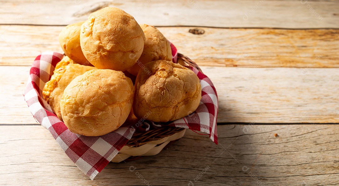 Pães de queijo em cesta sobre mesa de madeira
