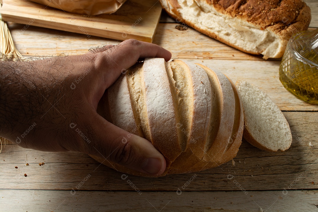 Homem cortando uma fatia de pão redondo em uma mesa de madeira