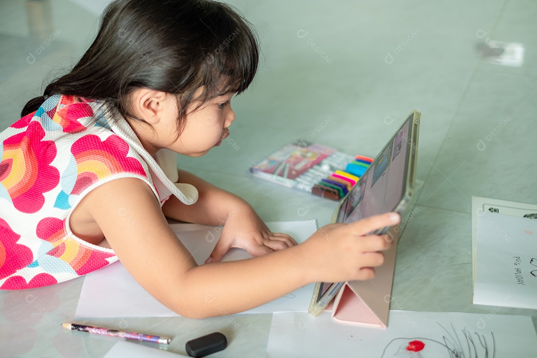 Menina asiática, de 5 a 6 anos, praticando origami usando videoclipes ou estudando on-line via tablet em casa
