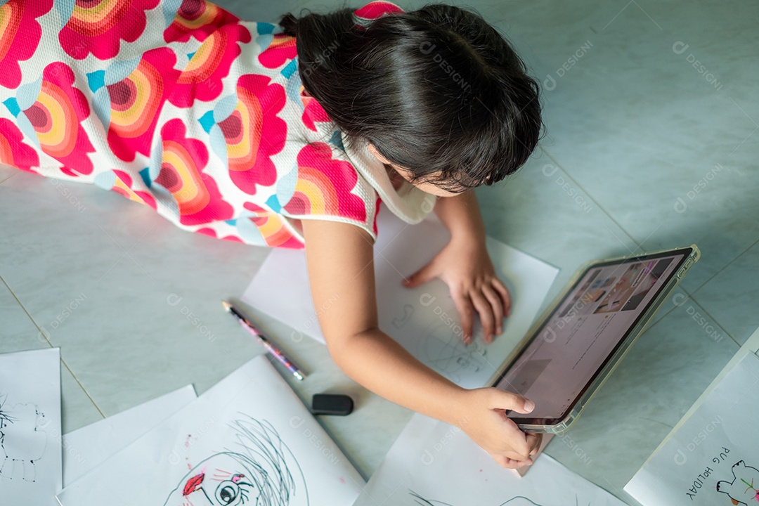 Menina asiática, de 5 a 6 anos, praticando origami usando videoclipes ou estudando on-line via tablet em casa